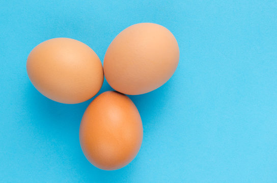 Three brown, chicken eggs blue background.