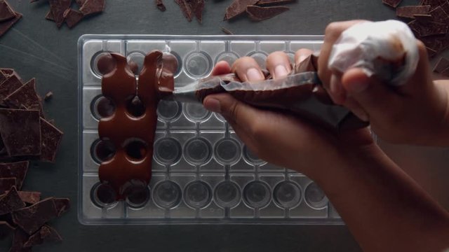 top view of hand with pastery bag filling candy mold. Liquid chocolate from top view