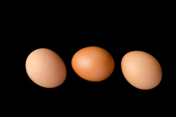 Three brown, chicken eggs black background.
