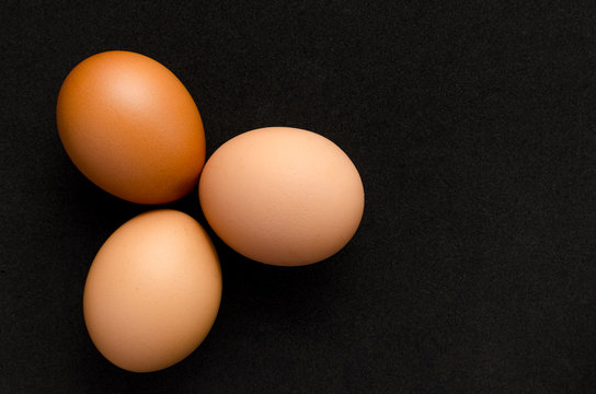 Three brown, chicken eggs black background.