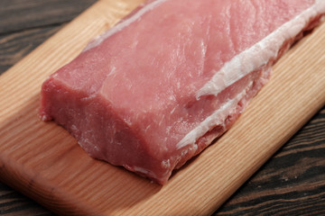 Whole boneless pork loin without fat close-up. Pork tenderloin on a cutting board on a dark background
