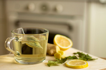 Herbal tea in a glass cup, black currant dried leaves, ginger and lemons, white kitchen interior at the background
