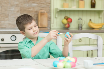 Fototapeta premium Little blond kid boy coloring eggs for Easter holiday in domestic kitchen