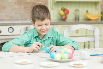 Little blond kid boy coloring eggs for Easter holiday in domestic kitchen