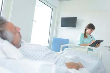 Fototapeta premium doctor taking notes from man patient lying in hospital bed