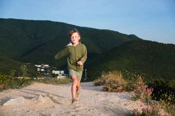 Six year old boy running on a mountain road at sunset with town view. Cool summer evening. Front view.