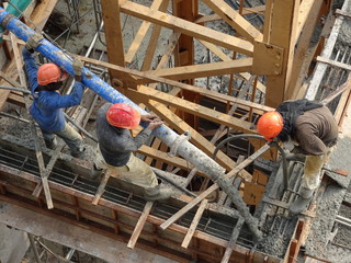 Construction workers pouring wet concrete using concrete spider hose into floor slab form work at...