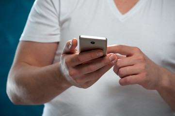 Close-up young man wearing casual clothes using smartphone on blue background.