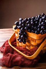 Photo of black grapes in wooden basket with claret cloth