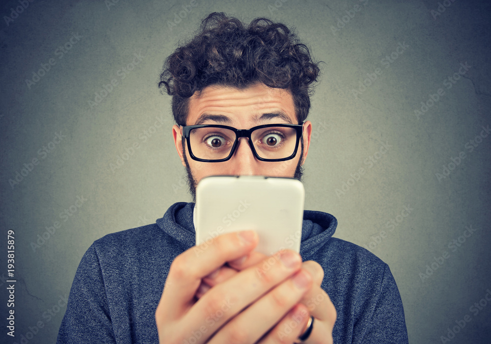 Wall mural shocked young man looking at smartphone