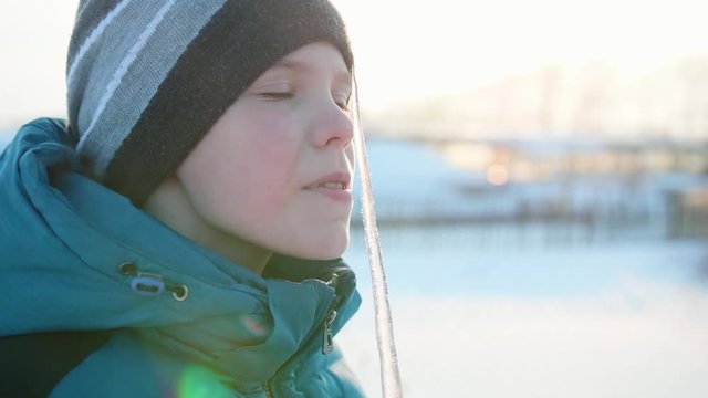 A boy licking an icicle. Snowy frosty Sunny day. Fun and games in the fresh air.