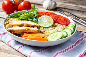 Healthy salad bowl with quinoa, tomatoes, chicken, cucumber, lime and arugula