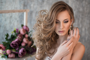 Fototapeta premium Portrait of a beautiful bride. Hands at the face. Wedding make-up. Volume hairstyle. The curls. Bouquet of flowers.