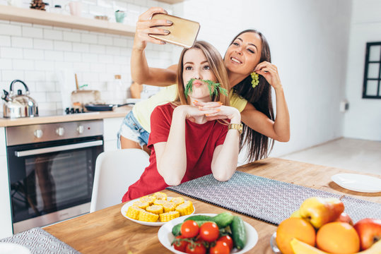 Women preparing food playing with vegetables in kitchen having fun and taking selfie.
