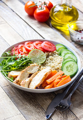 Healthy salad bowl with quinoa, tomatoes, chicken, cucumber, lime and arugula