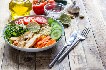 Healthy salad bowl with quinoa, tomatoes, chicken, cucumber, lime and arugula