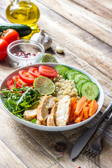 Healthy salad bowl with quinoa, tomatoes, chicken, cucumber, lime and arugula