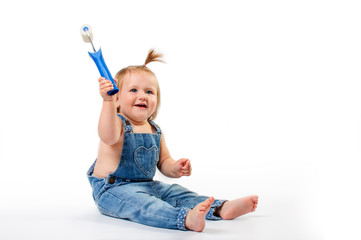 Little, cute baby girl dressed in denim overalls smiling and playing with paint roller