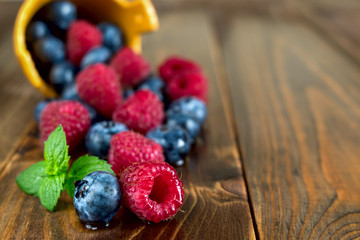 Berries of Blueberries and Raspberries, Poured from Basket, with Drops Water on Wooden Background.