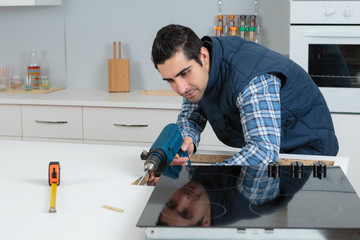 workman installing cooktop into kitchen