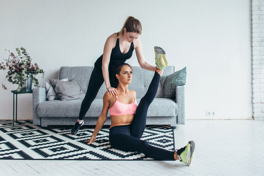 Fit woman doing stretching exercises with the help of friend holding her leg at home