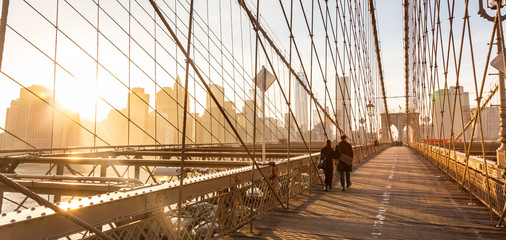 Couple walking on pedestrian path across Brooklyn bridge. New York City Manhattan downtown skyline...