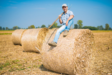 Smiling farmer sitting on an hay bale in his field