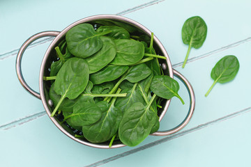 Baby spinach leaves in colander on blue wooden surface
