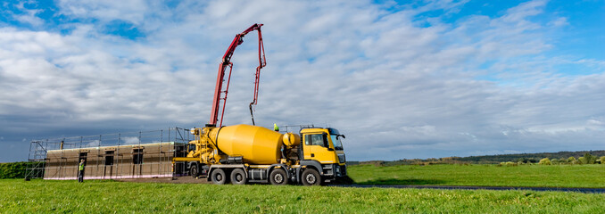 Wohnungsbau - gelber Betonmischer mit Betonpumpe vor einem Neubau