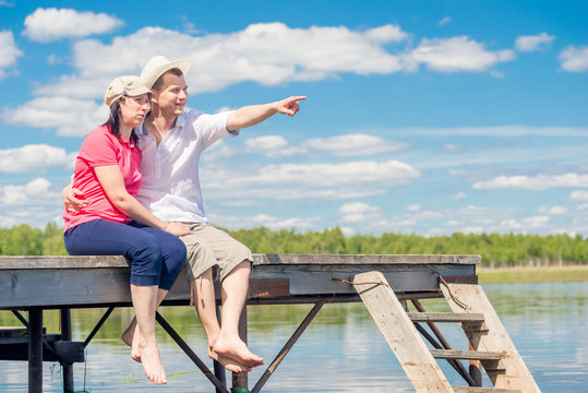 30-year-old couple resting on pier, man pointing at lake
