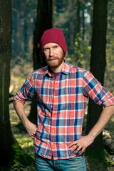 Naklejka na ściany i meble portrait of a serious man with a beard in a plaid shirt and hat in the woods