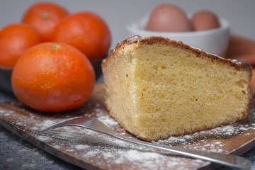 orange sponge cake on wooden plate on a table with tangerines and eggs