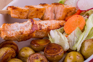 A shish kebab from trout pieces with pass potatoes baked is served with vegetable salad