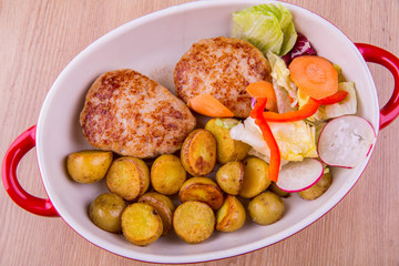 Chicken cutlets with pass potatoes roasted on coals, is served with lettuce leaves, a garden radish, red pepper, carrots