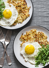 Large potato latkes, fried egg, arugula - tasty breakfast or snack on a gray background, top view