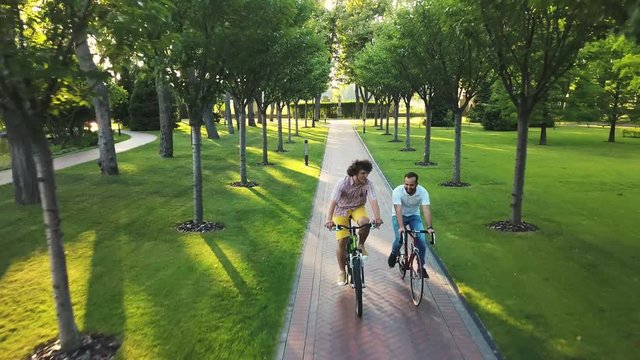 Two man cycling through park. Two male friends riding bicycles in public park, aerial view. People on vacation riding bicycles. Active summer weekend.
