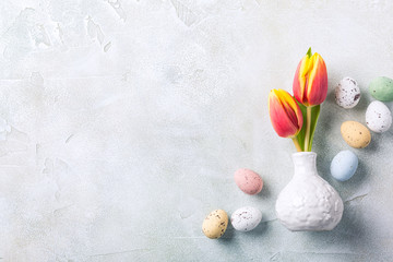 Obraz na płótnie Canvas Easter composition with spring tulips flowers in white vase and colored quail eggs candies. Holidays flat lay concept with copy space.