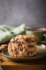 Stack of chocolate chip cookies on green plate with cup of coffee on old wooden table. Selective focus. Copy space.