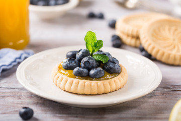 Homemade shortbread tartlet with lemon curd and fresh blueberries on white wooden background. Holiday food concept.
