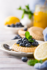 Homemade shortbread tartlet with lemon curd and fresh blueberries on white wooden background. Holiday food concept with copy space.
