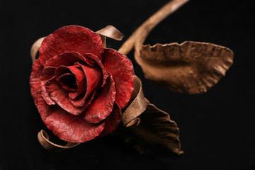 The fine rose made by a forging method of metal with a red blossom and a stalk of bronze color. Close up.