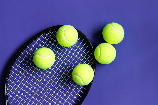 Tennis balls on black racket. Violet background. Concept sport.