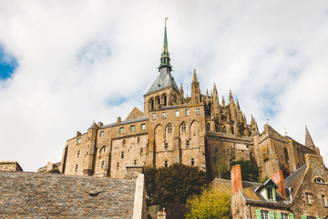 Low view of abbey with statue of Archangel Michael on spire on Le Mont Saint-Michel island famous for its low tide, in Normandy, France