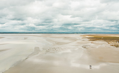 Fototapeta na wymiar Unidentified people walking on sands during low tide outside Le Mont Saint-Michel tidal island in Normandy, France