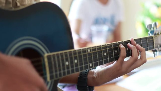 Young Man Student Practicing playing guitar with his friend sitting on table in classroom.