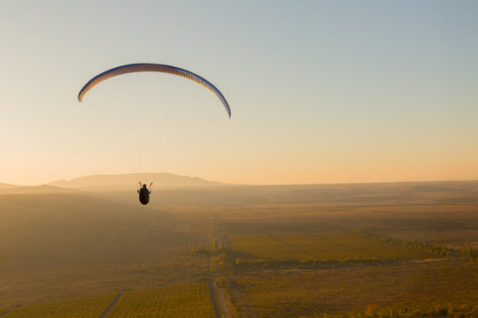 Paraplan flying over a field at sunset