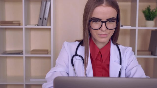 portrait beautiful caucasian doctor working with computer. therapist reading medical records or search some information use internet. candid woman wearing white medical coat with stethoscope indoors