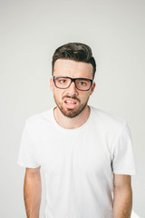 Obraz premium A portait of a guy in white t-shirt and glasses looking straight to camera. His sight is strange and disturbed. Close up.