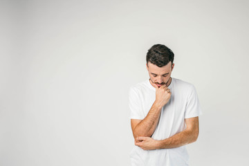 Obraz premium A picture of thoughtful and serious dark-haired man standing on the right side of frame and thinking. He has put his left arm on the elbow and holding his chin with a right hand.