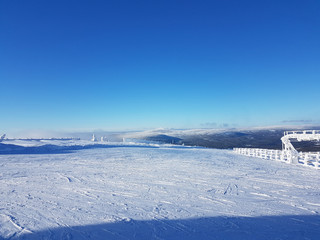 Top of a snowy mountain used as skiing resort, with blue sky and tracks from the skiers